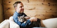 person cuddling cat on white couch in front of wood slat wall