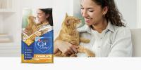 A woman smiles and looks down at an orange tabby cat; to the left sits a bag of Purina Cat Chow Complete Chicken