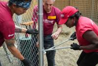Three volunteers putting together a chain-link fence