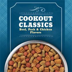 A close-up of a bowl of kibble sits on a blue patterned background. Text reads "Cookout Classic Beef, Pork and Chicken Flavors"