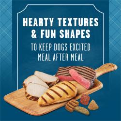 Slices of cooked beef steak and chicken breasts are presented on a wooden cutting board, accompanied by enlarged pieces of kibble. Text reads "Hearty textures and fun shapes to keep dogs excited after every meal"