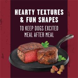 A sliced beef steak is presented on an iron skillet, garnished with parsley and three pieces of kibble. Text reads "Hearty textures and fun shapes to keep dogs excited after every meal"