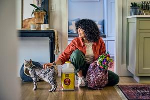 woman sits in her house petting her cat next to a jug of Purina Tidy Cats cat litter.
