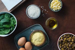 Assortment of pet food ingredients including vegetables, grains, eggs and oils arranged on a tabletop.