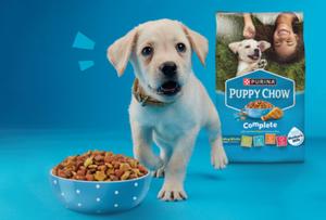 puppy barking in front of a bowl of Puppy Chow food and next to the package