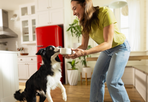 Woman feeding her dog healthy Purina ONE fresh dog food from a white bowl.