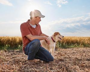 A farmer kneels in a field next to his dog.