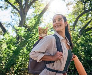 A young woman hikes with her cat safely carried in her backpack.