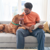 Person sitting on a couch using a tablet while a brown dog rests beside them and looks up