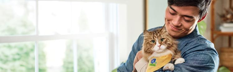 A man smiles as he holds a fluffy tan and white cat wearing a yellow bandana