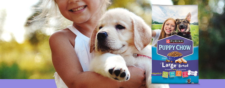 young girl holding a white puppy next to a Puppy Chow Large Breed dry food bag