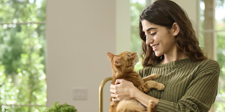 A woman stands in a kitchen while snuggling an orange tabby cat
