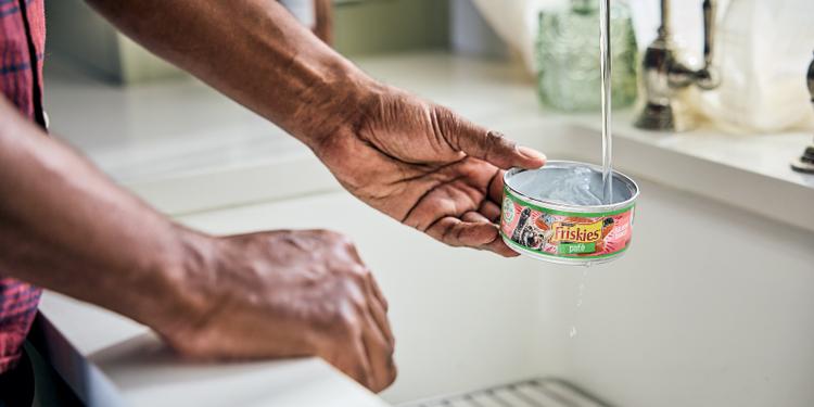 person rinses out a can of Friskies wet cat food to prepare it for recycling.
