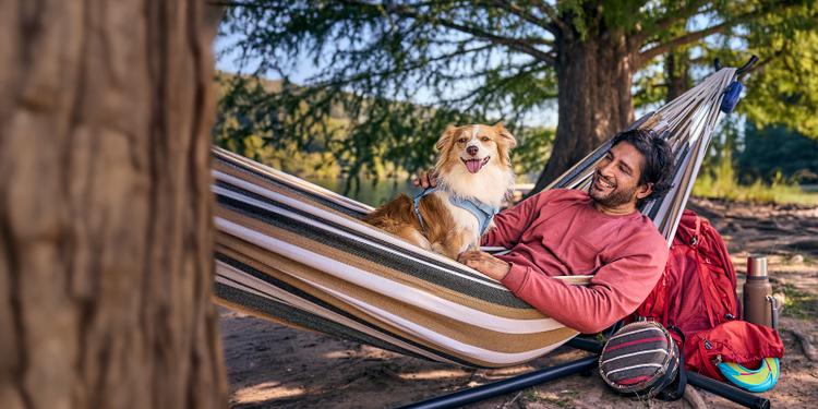 A man lounges in a hammock with his happy dog.
