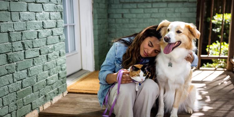 Woman sitting on steps snuggling a dog and cat