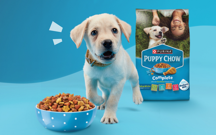 puppy barking in front of a bowl of Puppy Chow food and next to the package
