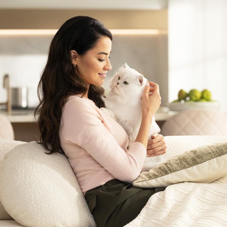 Woman on a couch cuddling with a fancy feast white cat