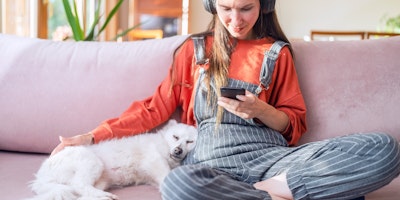 person sitting on couch with headphones on and sitting next to sleeping white dog