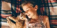 young girl laying with orange tabby kitten