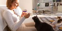 owner feeding cat from yogurt cup