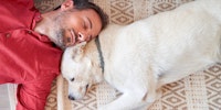 Male dog owner nuzzles dog’s head while laying on floor