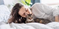 una persona tumbada en la cama besando a un gato con rayas grises