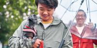 man with umbrella looking down and smiling at a small grey dog