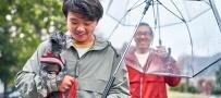 Un hombre sosteniendo un perro y un hombre parado bajo la lluvia