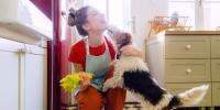 Dog licking woman in kitchen who is holding a bunch of celery