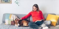 person in red shirt sitting on couch petting a sleeping dog