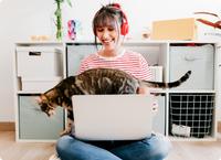 Mujer sentada en el suelo con auriculares rojos con gato caminando en su computadora portátil