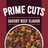 A close-up of a bowl of kibble sits on a maroon and brick red background. Text reads "Prime Cuts Savory Beef Flavor"