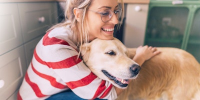 woman smiling while hugging a golden retriever dog