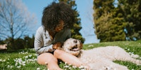 woman sitting in the grass with a dog laying back on her lap