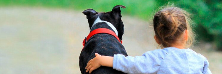 child and dog friends sitting on the ground. The child has their arm around their dog