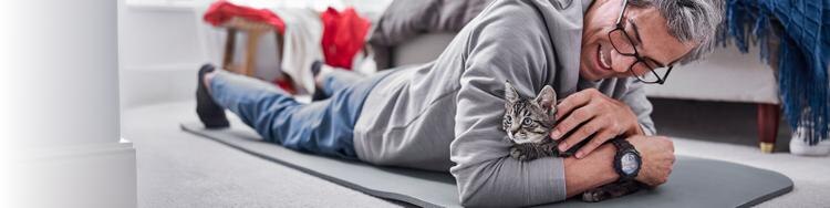 A kitten being held and pet by its owner while laying on a yoga mat