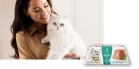 Woman holding white cat with Fancy Feast Gems package in front of image