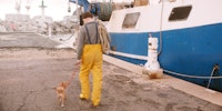 A man walking a dog on a leash at a boat dock