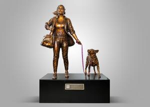 una estatua que representa a una mujer con maletas hechas, con un perro a su lado con correa